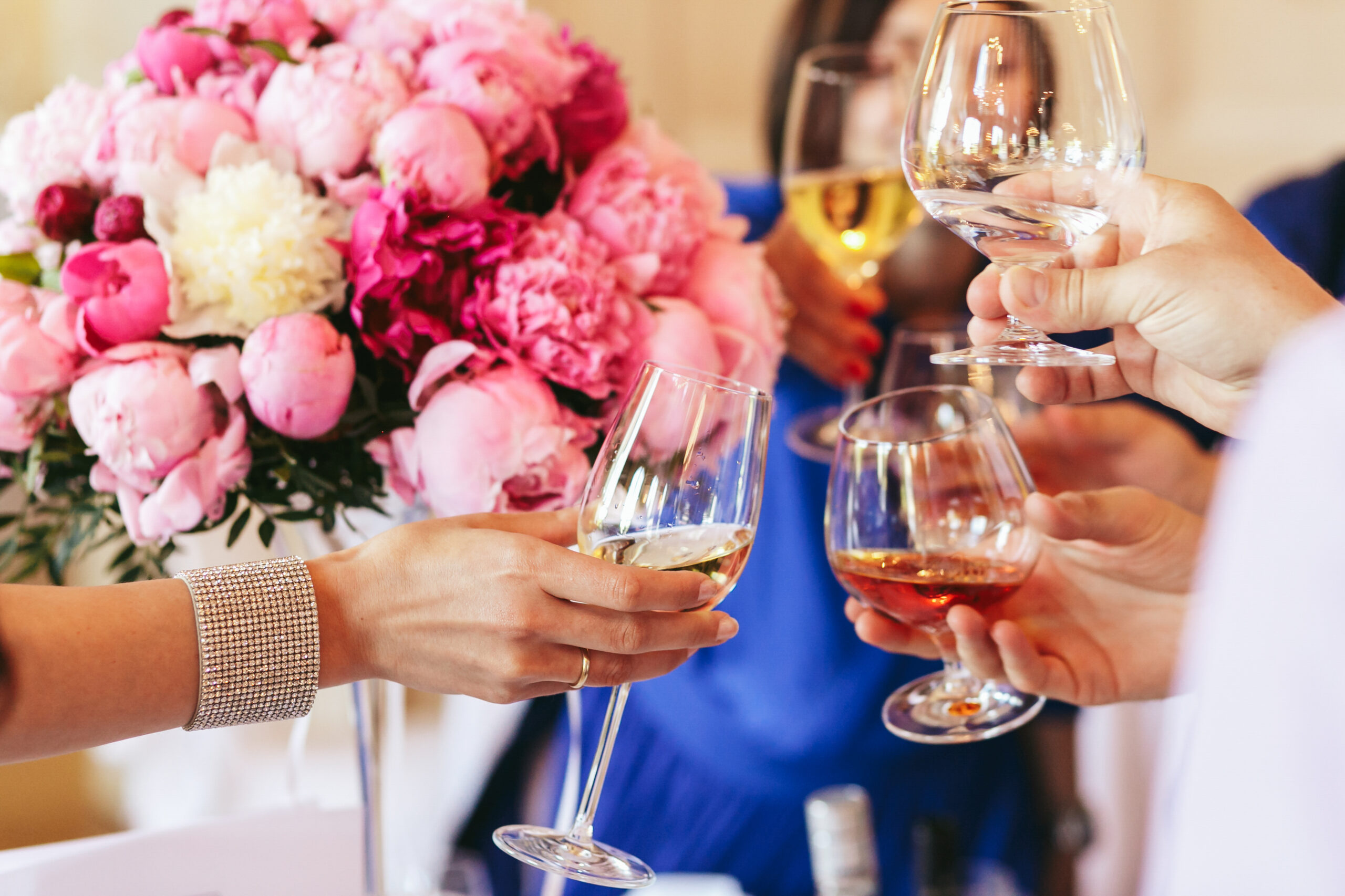 Guests clang glasses of champagne and whisky before a pink bouquet